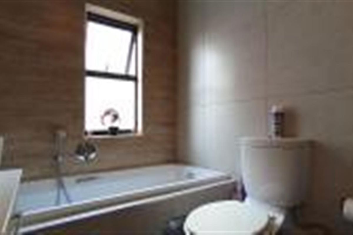 A functional bathroom featuring a bathtub, toilet, and neutral wall tiling with a window for natural light.