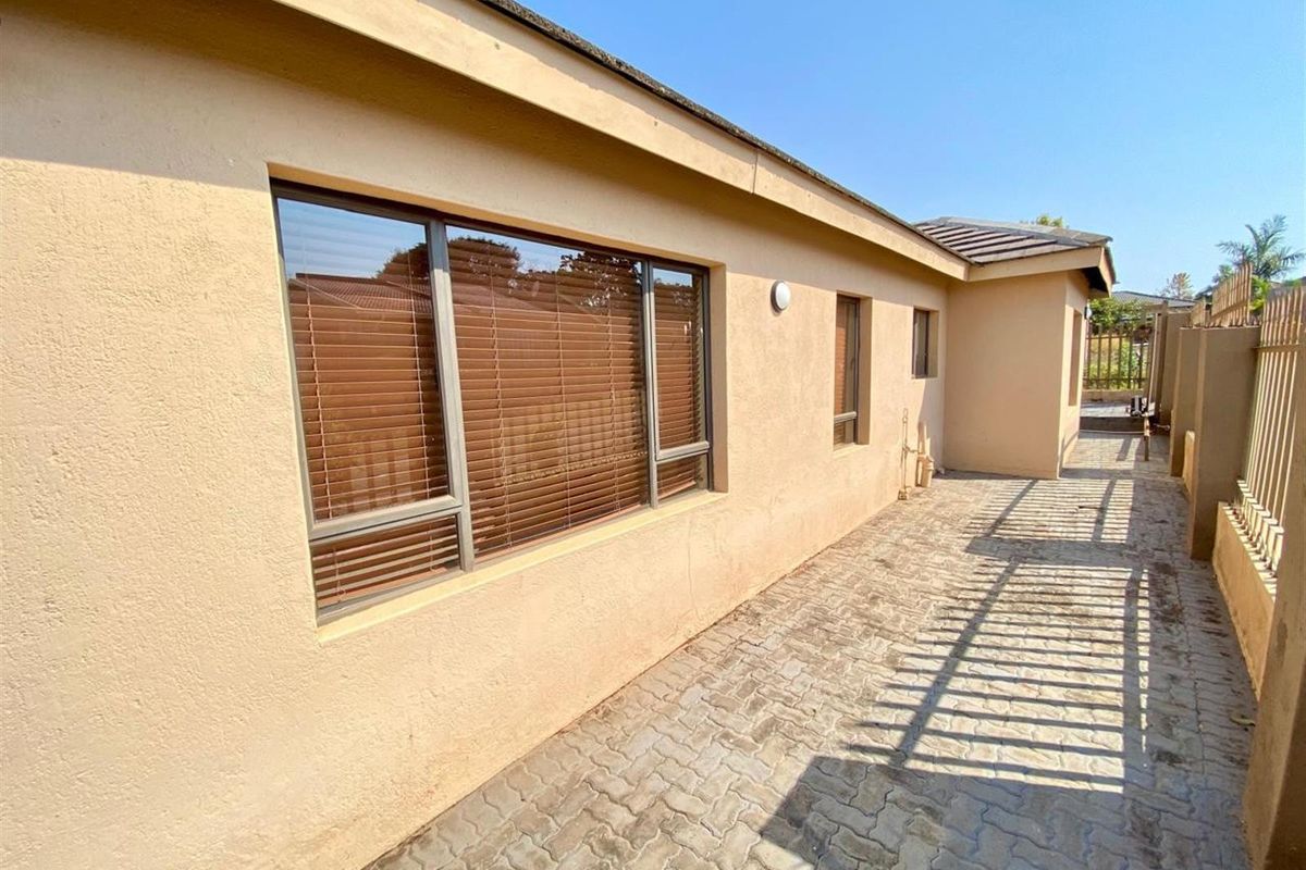A side exterior view of the house featuring paved walkways, plastered walls, and window blinds.