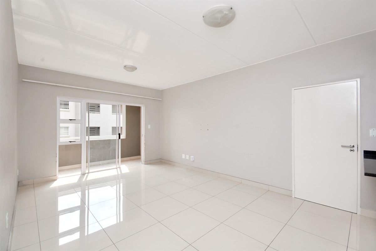 A bright, empty living room featuring neutral tiled flooring, clean white walls, and a sliding glass door providing access to an outdoor area.