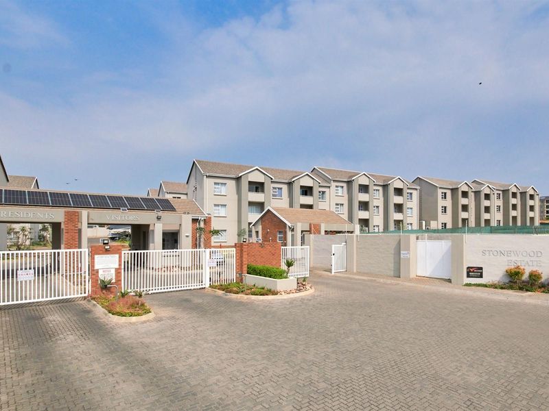 The main entrance to Stonewood Estate featuring a secure gated access point, paved driveway, and brick boundary walls with integrated solar panels.