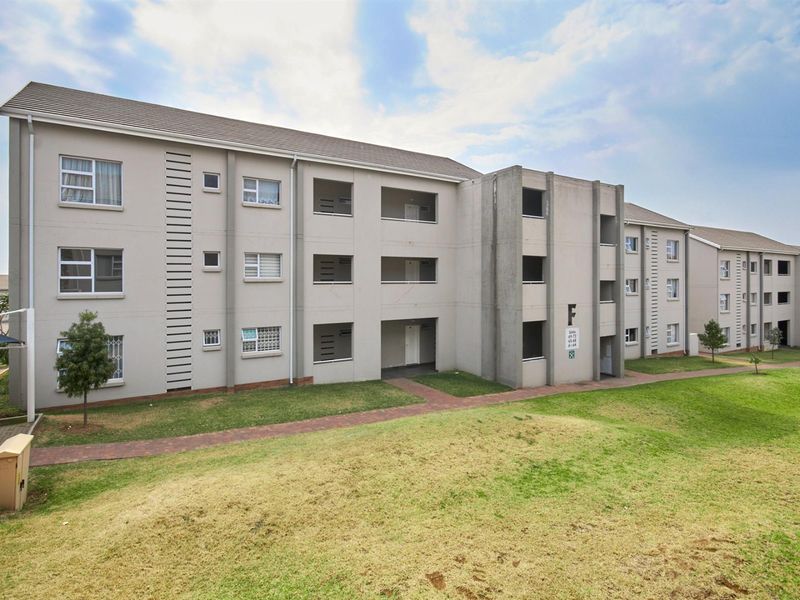 Exterior view of a multi-story apartment block featuring a tiled roof, paved walkways, and private balconies.