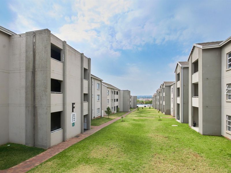 View of the apartment complex grounds featuring paved walkways, well-maintained lawns, and multi-story residential blocks with exterior concrete finishes.