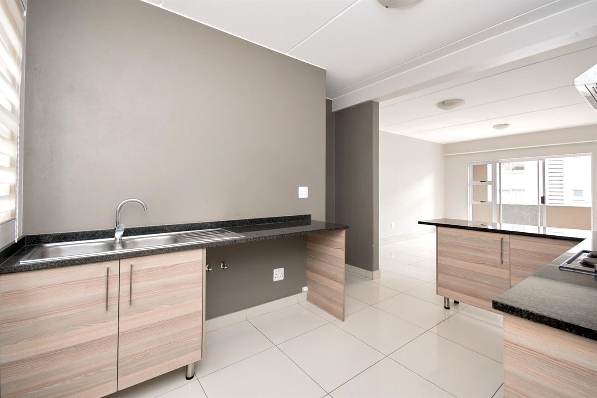 Modern kitchen featuring light wood-finish cabinetry, dark granite countertops, stainless steel sink, and tiled flooring in an open-plan layout.
