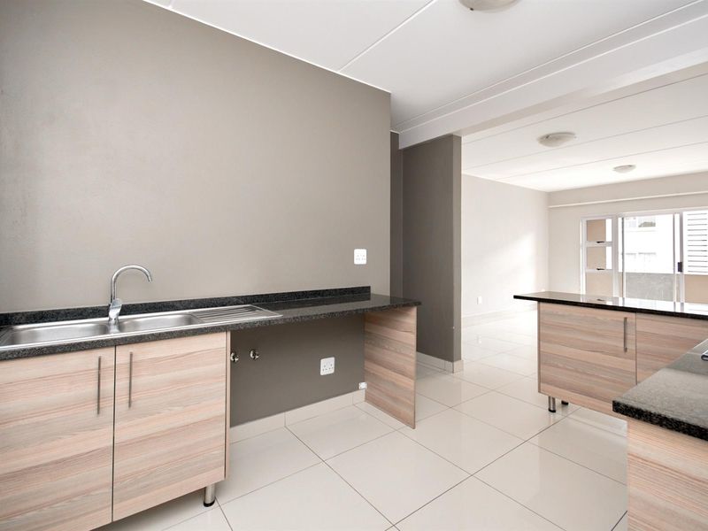 Modern kitchen featuring light wood-finish cabinetry, dark granite countertops, stainless steel sink, and tiled flooring in an open-plan layout.