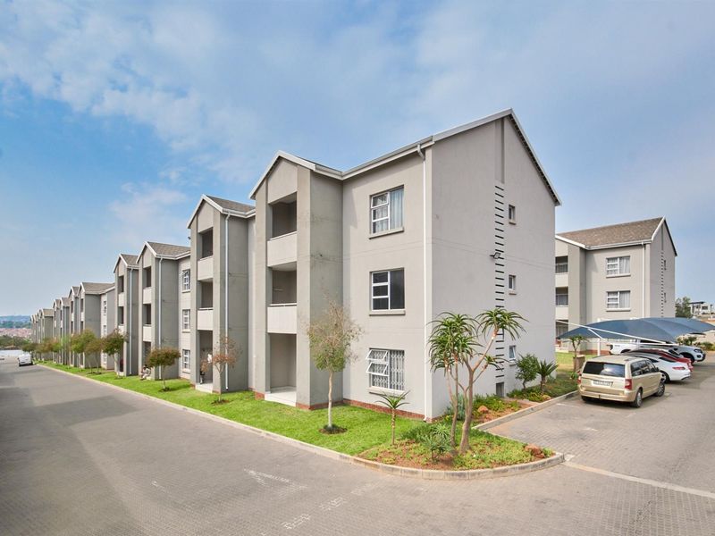 Exterior view of a multi-story apartment complex featuring paved driveways, covered parking bays, and landscaped garden areas.