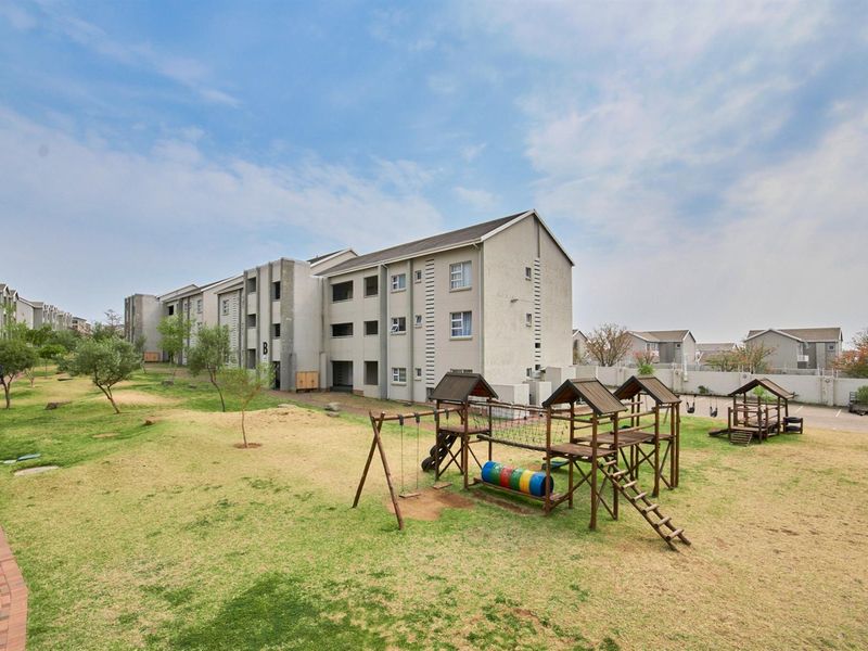 Exterior view of the apartment complex featuring a communal garden area with a playground and paved walkways.