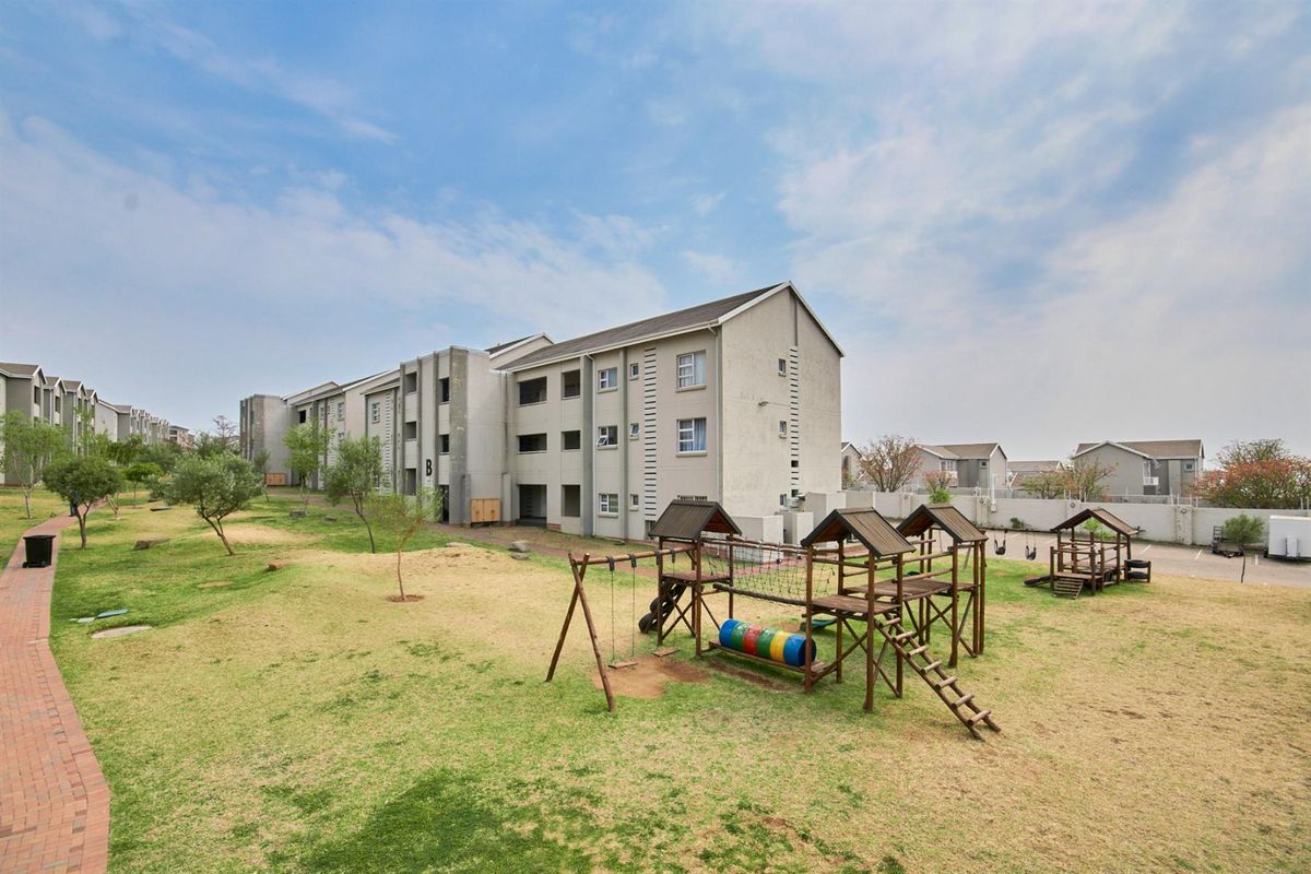 Exterior view of the apartment complex featuring a communal garden area with a playground and paved walkways.