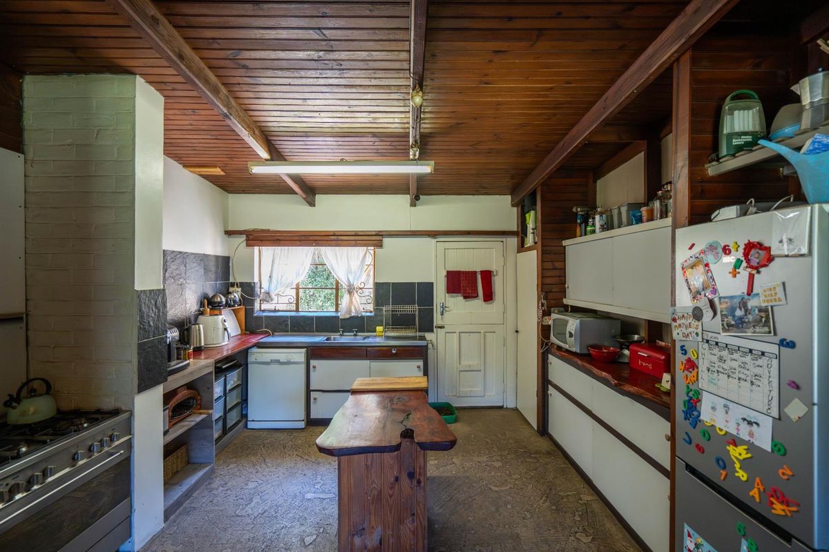 A rustic kitchen featuring exposed timber ceiling beams, built-in cabinetry, a gas stove, and a central wooden island bench.