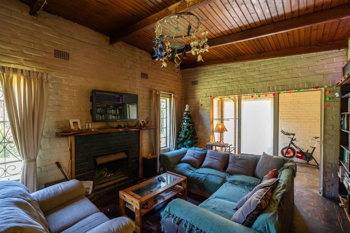 Living room featuring a brick fireplace, exposed timber beam ceiling, and parquet flooring with access to an adjacent sunroom area.