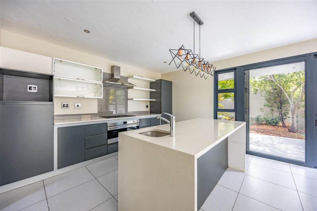 Modern kitchen featuring a central island with sink, built-in oven, gas hob, extractor fan, and sleek cabinetry, opening directly to a private garden patio.