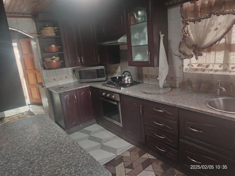 A functional kitchen featuring dark wood cabinetry, granite countertops, a built-in oven with gas hob, and tiled flooring.