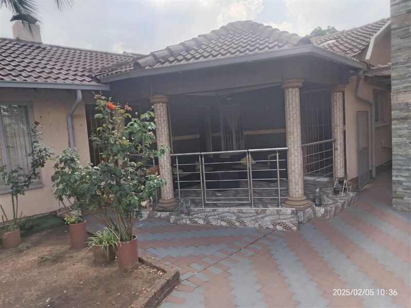 A covered patio area featuring decorative columns, stainless steel balustrades, and tiled flooring, overlooking a paved outdoor space.