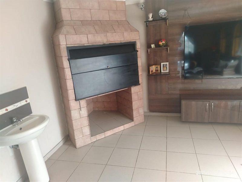 Living area featuring a built-in brick fireplace, tiled flooring, and a convenient pedestal basin, offering a functional space for relaxation and entertainment.