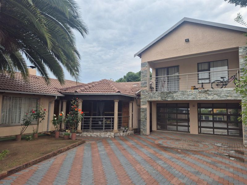 Front elevation of a two-story house featuring a paved driveway, double garage, covered patio, and an upper-level balcony with stainless steel railings.