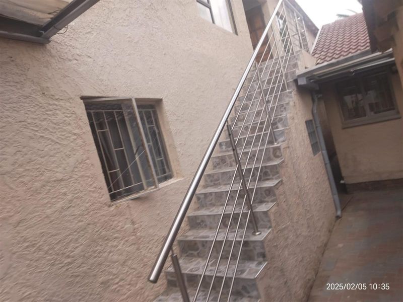 Exterior view of a rear courtyard featuring an external staircase with stainless steel balustrades and tiled steps leading to an upper level.