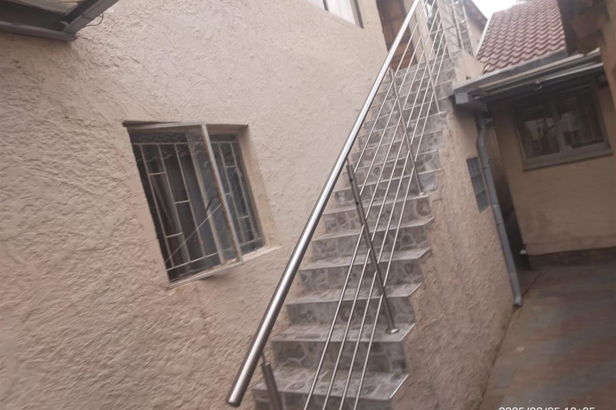 Exterior view of a rear courtyard featuring an external staircase with stainless steel balustrades and tiled steps leading to an upper level.