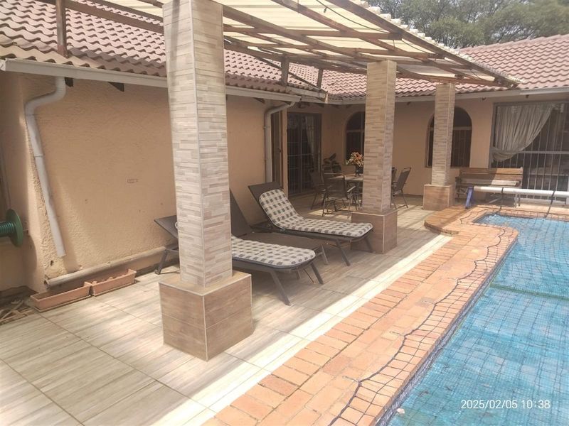 A covered patio area featuring tiled columns and flooring, overlooking a swimming pool with brick coping and a safety net.