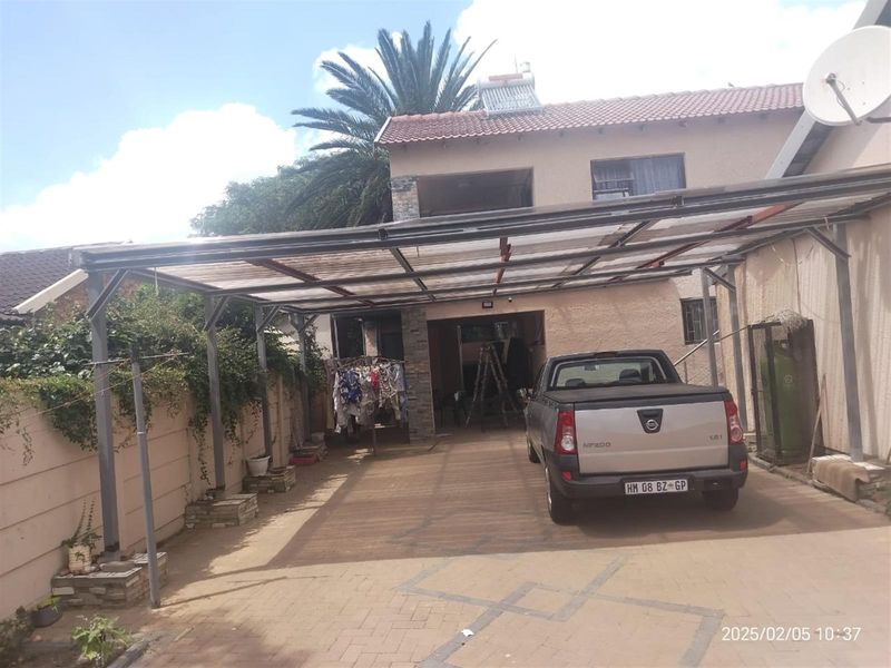 Front exterior view of the property featuring a paved driveway, a large metal carport structure, and a solar water heating system on the roof.