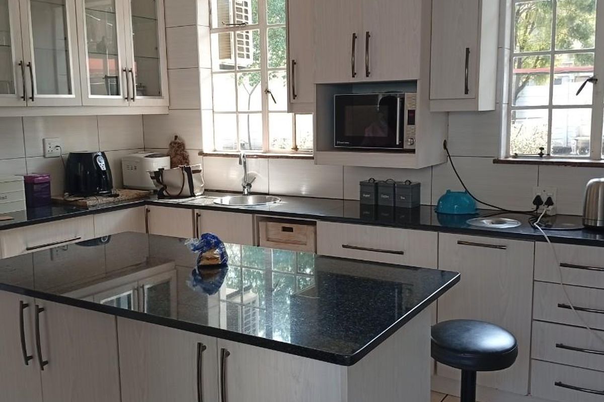 A functional kitchen featuring light wood-grain cabinetry, dark granite countertops, a central island, and tiled flooring with ample natural light.