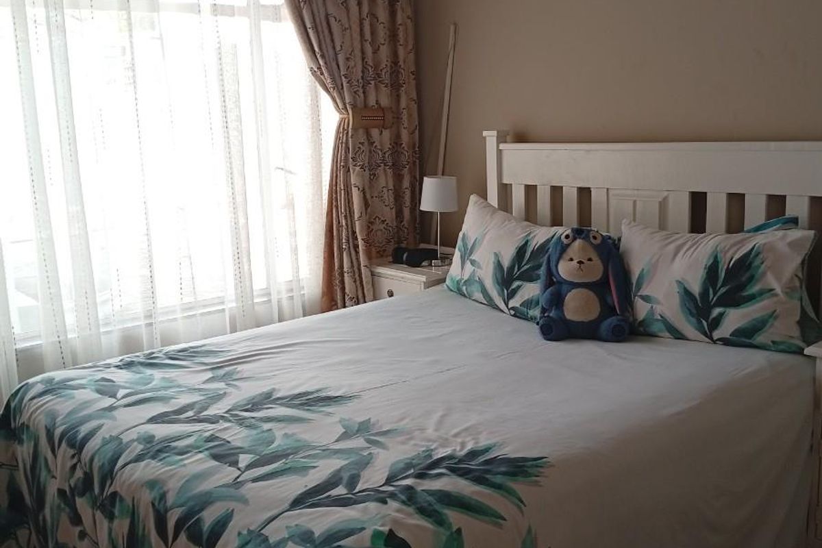 A cozy bedroom featuring a large window with layered curtains, providing natural light and a comfortable living space.