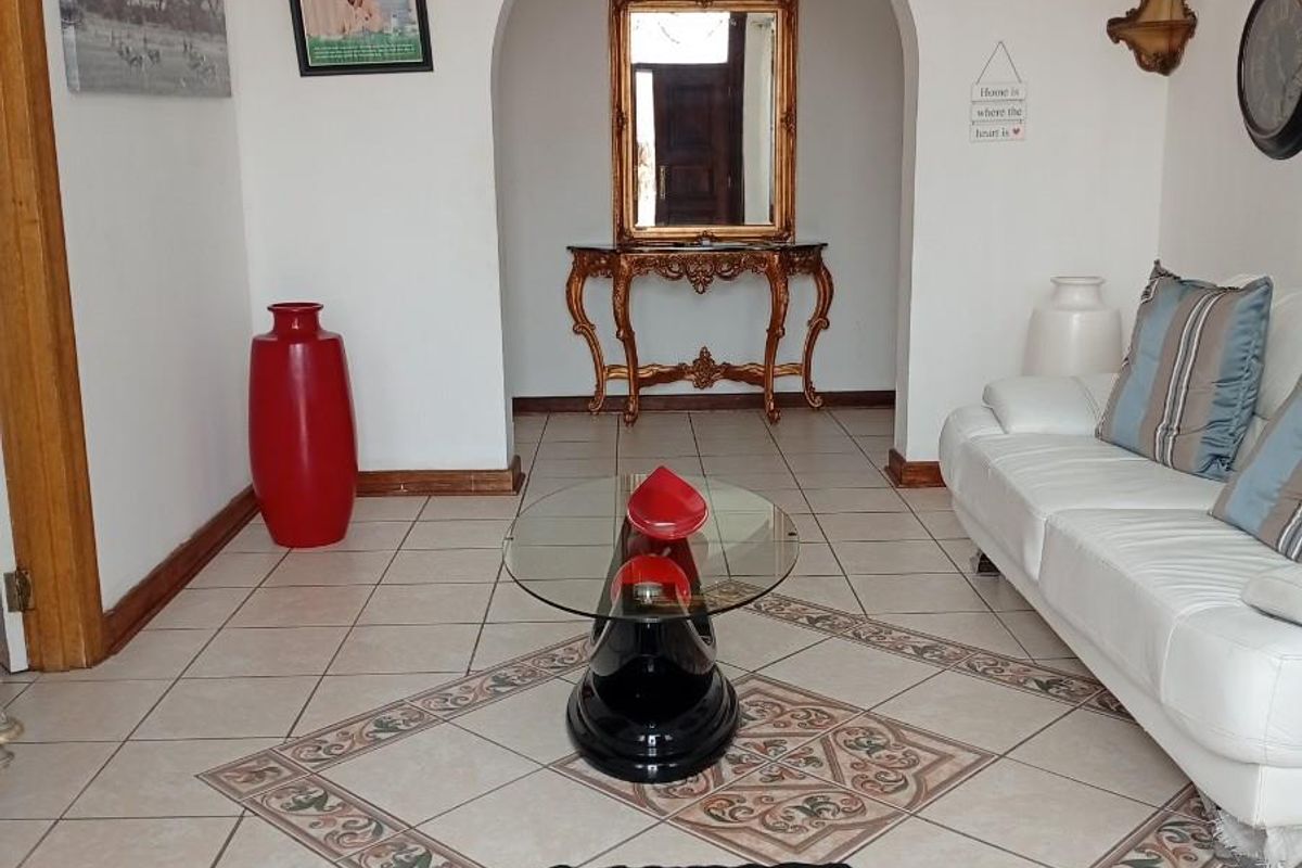 A bright living area featuring decorative ceramic floor tiles with a central inlay, an arched entryway, and crown molding.