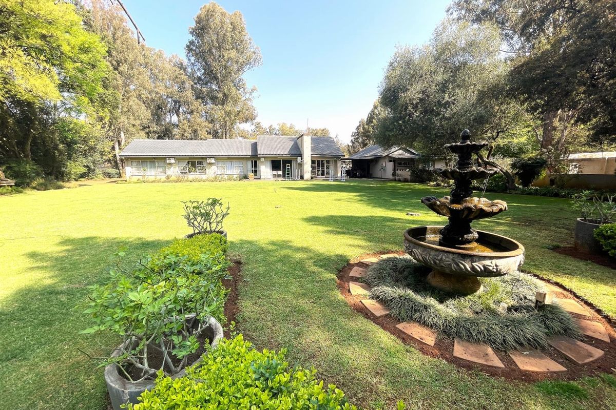 Spacious rear garden featuring a tiered stone fountain, manicured lawn, and mature trees, providing a serene outdoor setting for the property.