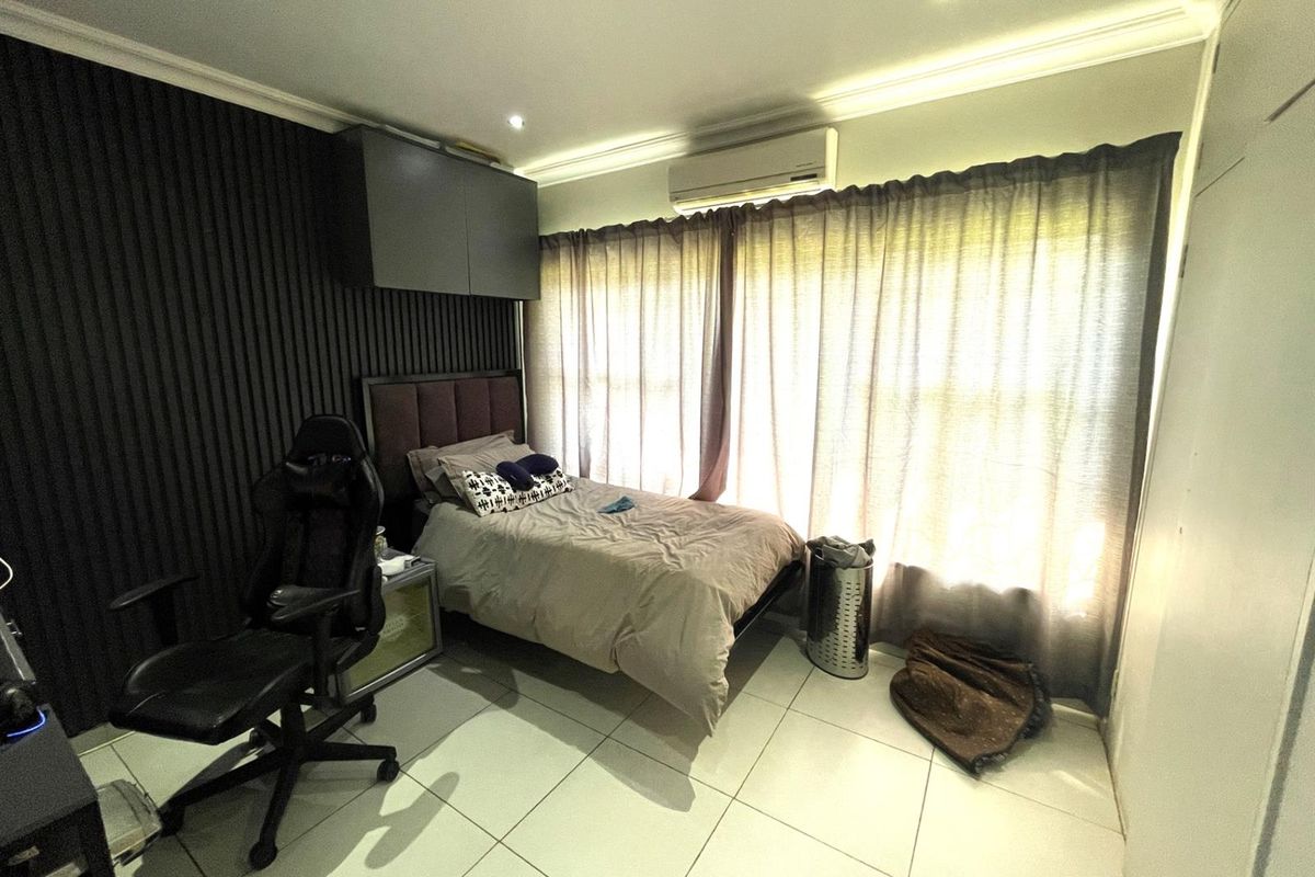 A bedroom featuring tiled flooring, a dark slatted feature wall, built-in cabinetry, and a wall-mounted air conditioning unit.