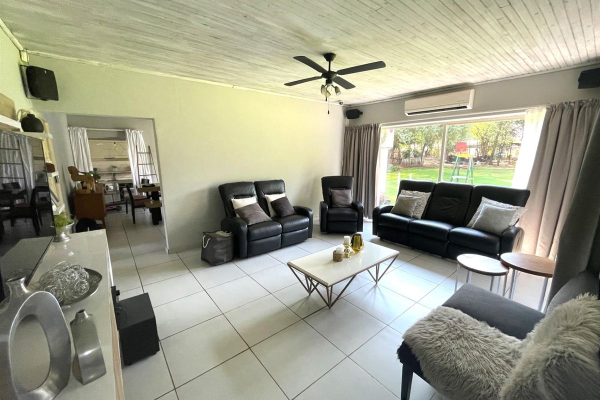 Spacious living room featuring large windows, a ceiling fan, and a wall-mounted air conditioning unit, with direct access to the garden area.