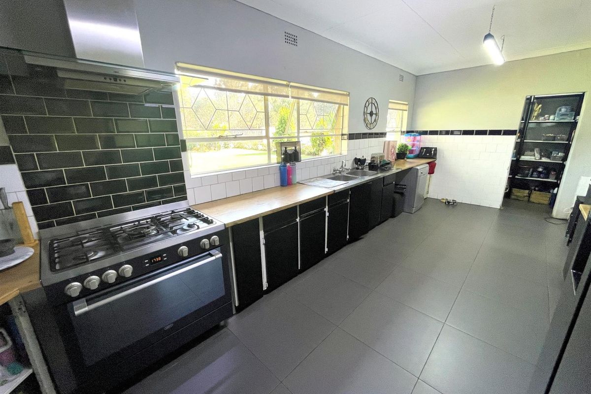 Modern kitchen featuring dark cabinetry, a gas stove with extractor fan, tiled splashbacks, and a spacious countertop with a double sink.