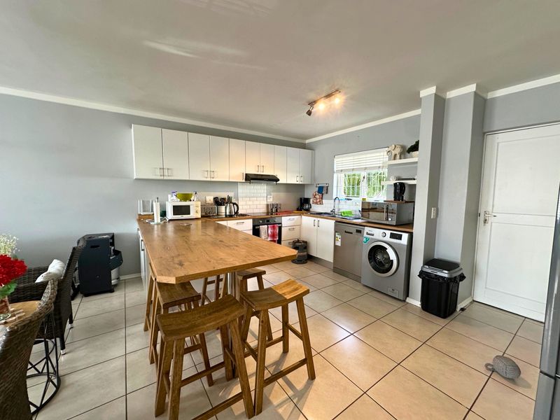 A functional kitchen featuring white cabinetry, subway tile backsplash, integrated appliances, and a wooden breakfast bar, finished with neutral tiled flooring.