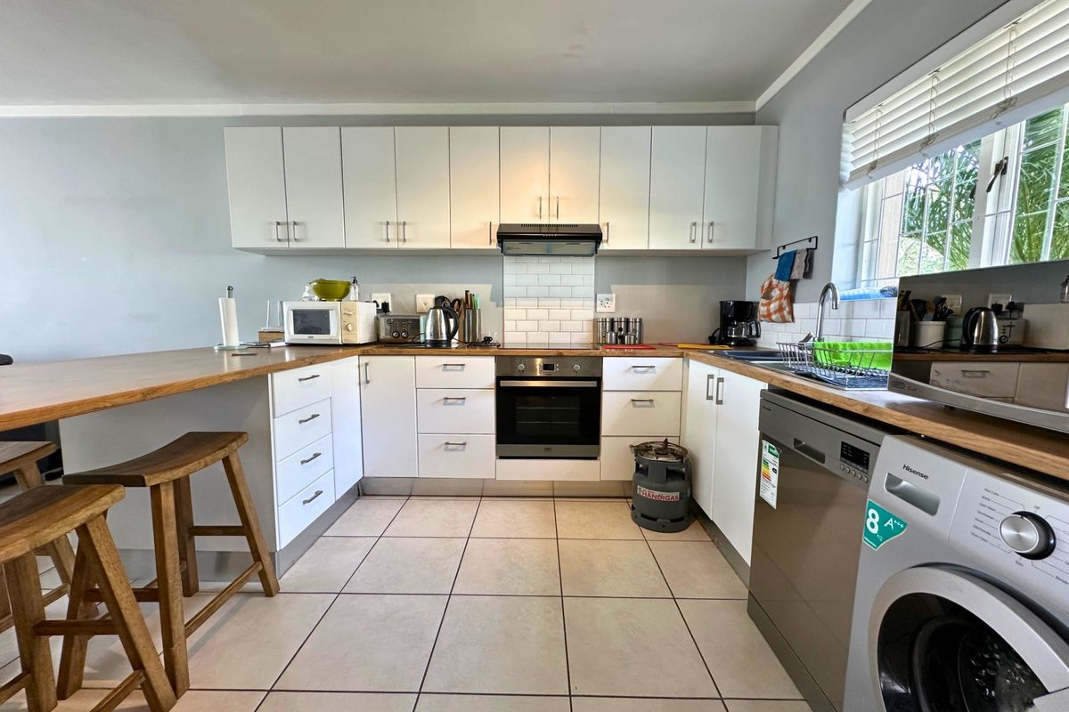 A functional kitchen featuring white cabinetry, wooden countertops, subway tile backsplash, built-in oven, extractor fan, and tiled flooring with an integrated breakfast bar.