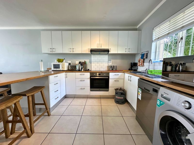 A functional kitchen featuring white cabinetry, wooden countertops, subway tile backsplash, built-in oven, extractor fan, and tiled flooring with an integrated breakfast bar.