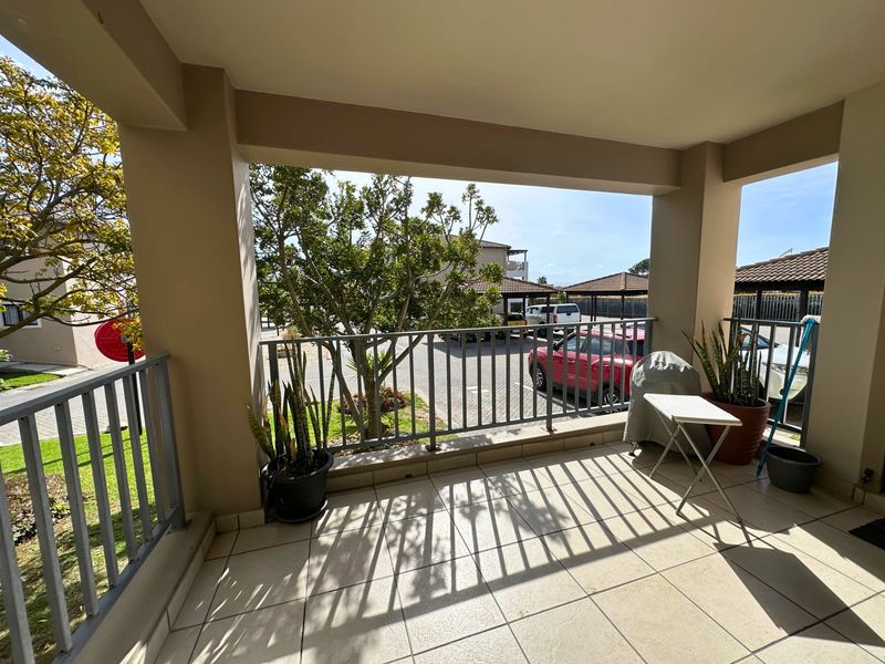 A covered balcony featuring tiled flooring and a metal balustrade, offering an outdoor space with views of the complex grounds.