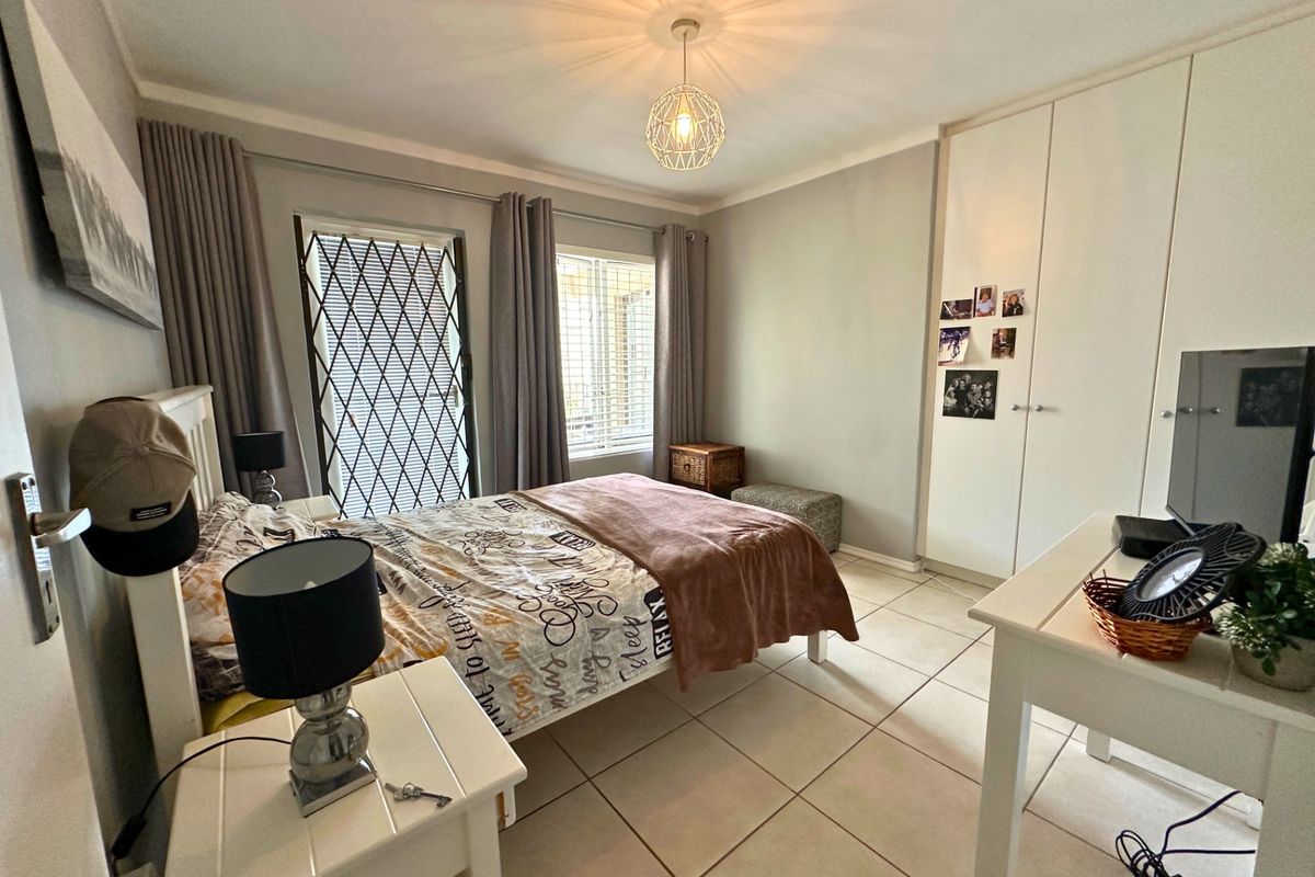 A well-maintained bedroom featuring neutral tiled flooring, built-in cupboards, and a security gate leading to an outdoor area.