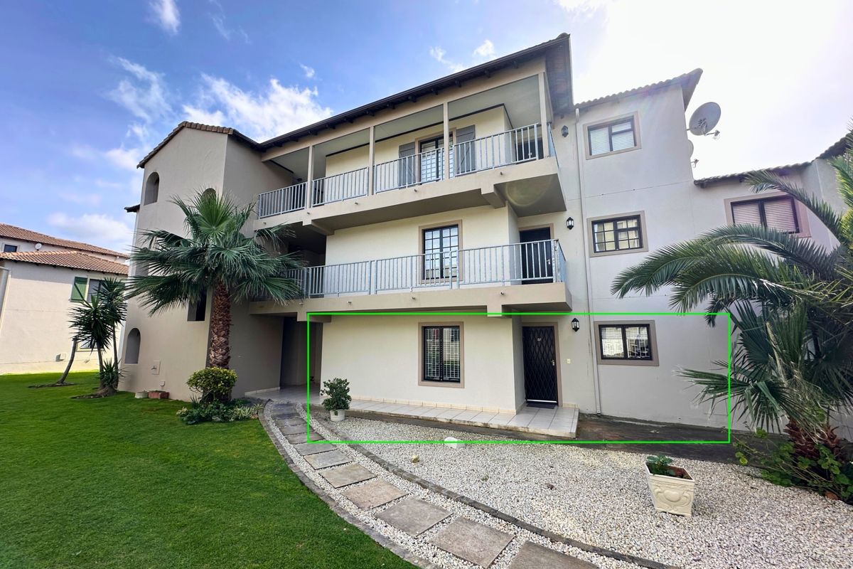 Rear view of a multi-story apartment building featuring balconies, a ground-floor patio, and well-maintained communal garden areas with paved walkways.