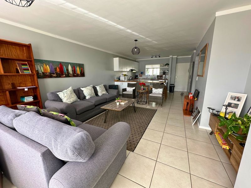 Open-plan living and kitchen area featuring neutral tiled flooring, modern cabinetry, and a breakfast counter, creating a functional and connected living space.