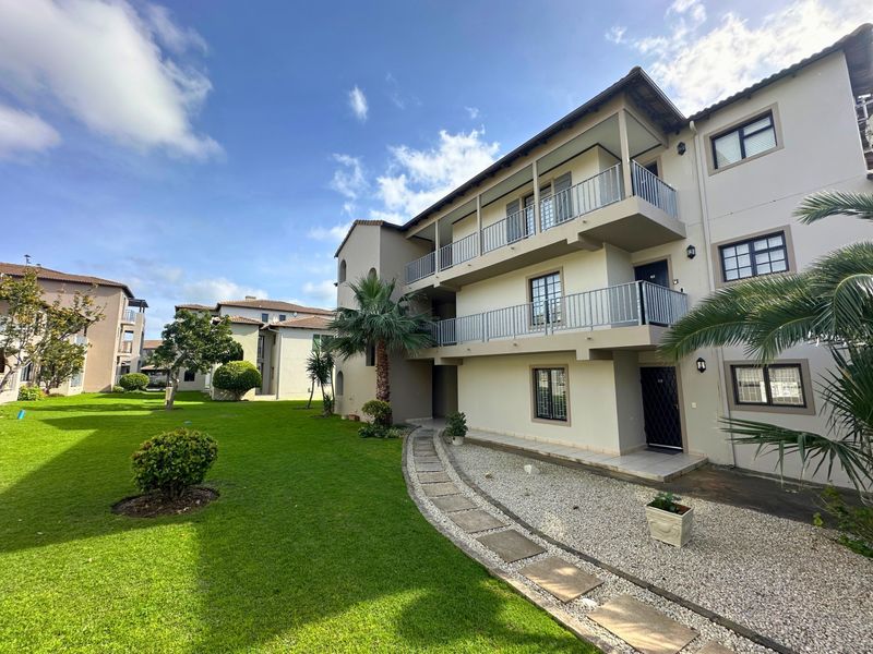 Exterior view of a multi-story apartment complex featuring private balconies, a well-maintained lawn, and paved walkways within a landscaped residential estate.
