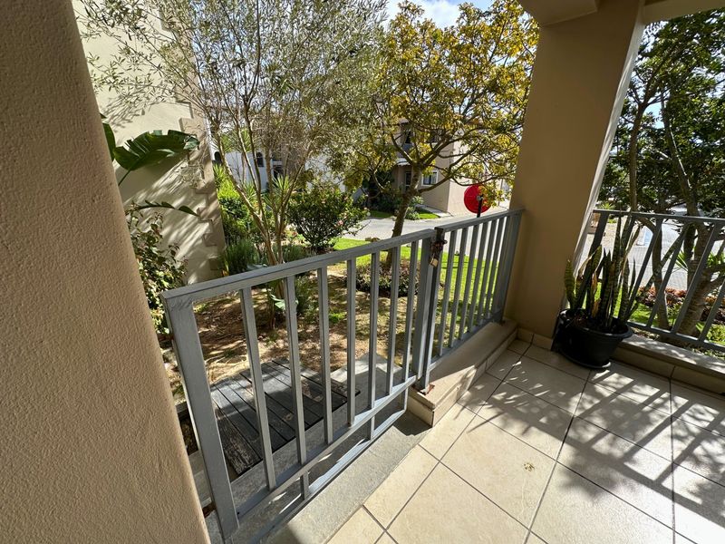 A covered ground-floor patio featuring tiled flooring and a metal balustrade with a gate providing direct access to the garden area.