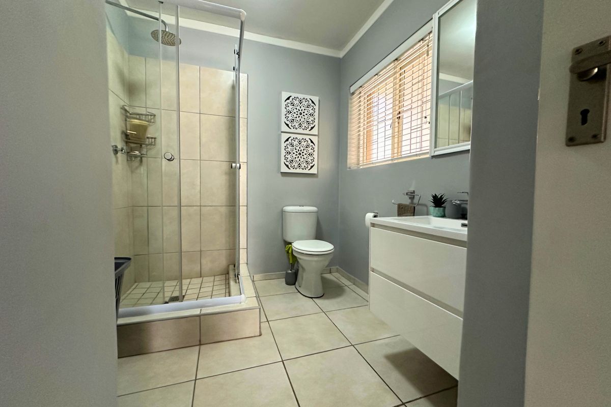 A clean, modern bathroom featuring a glass-enclosed shower, a wall-mounted vanity with basin, and neutral floor tiling.