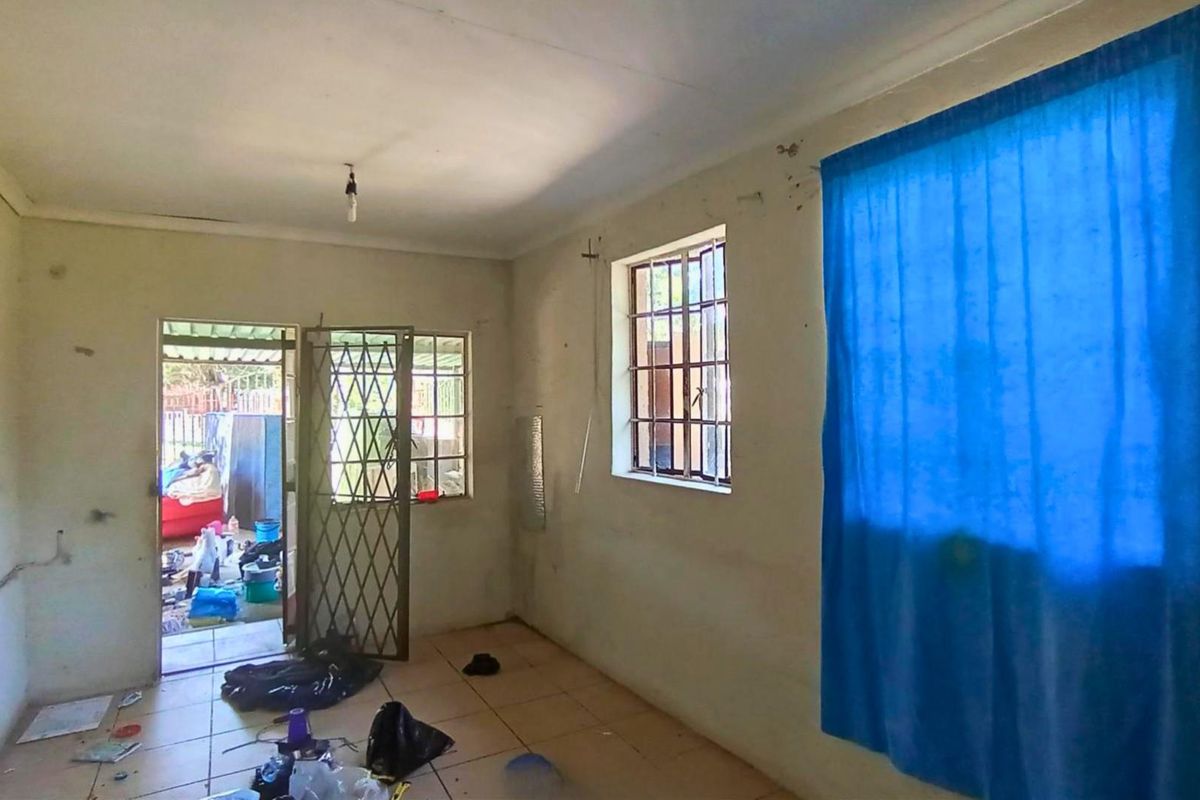 A basic living room area featuring tiled flooring, security gates, and window burglar bars, requiring cosmetic updates and maintenance.