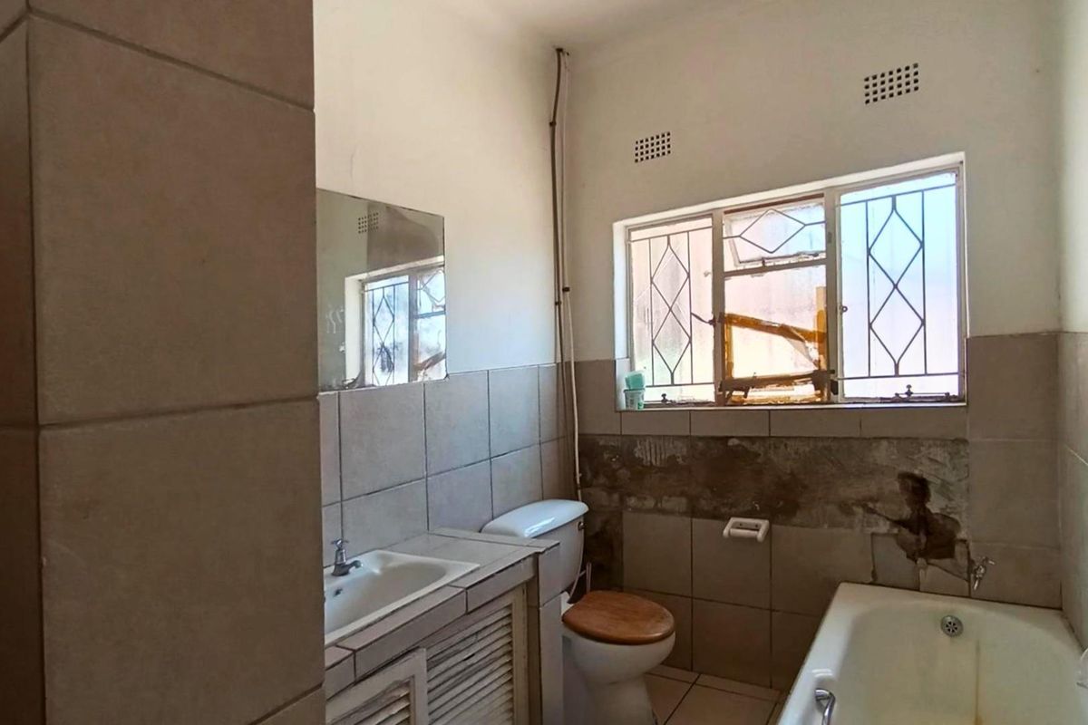 A dated bathroom featuring a built-in vanity, toilet, and bathtub, currently requiring significant renovation and repair to wall finishes and fixtures.