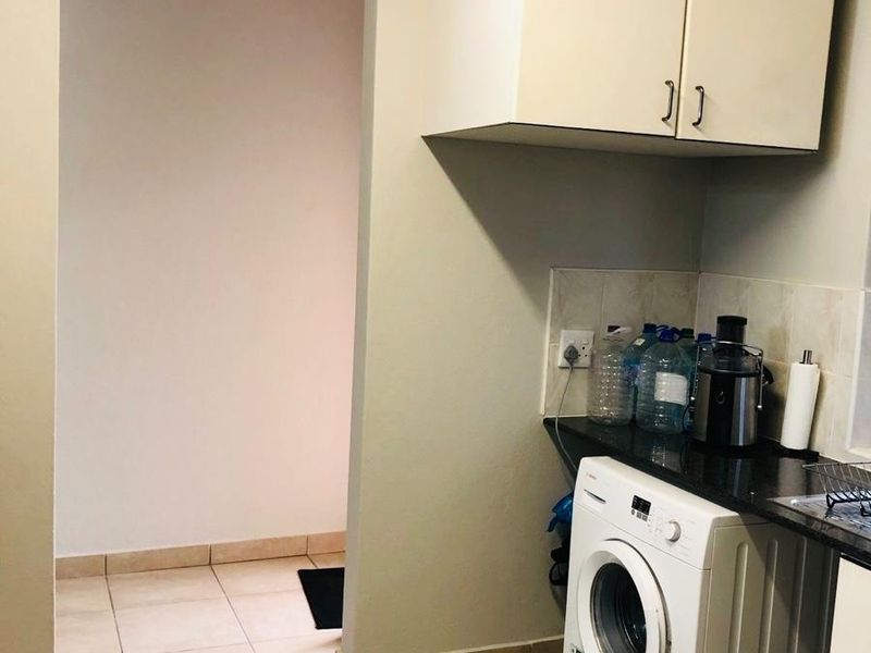A functional laundry area featuring built-in cabinetry, a dark countertop, and space for a washing machine with tiled flooring.