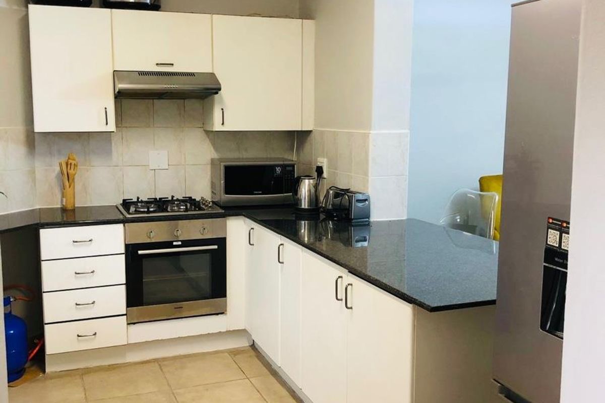 A functional kitchen featuring white cabinetry, dark granite countertops, a built-in oven, gas hob, and extractor fan with tiled flooring.