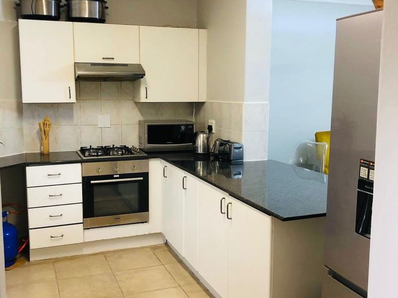 A functional kitchen featuring white cabinetry, dark granite countertops, a built-in oven, gas hob, and extractor fan with tiled flooring.