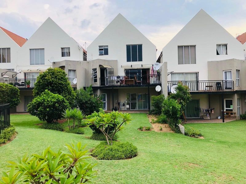 Rear view of a multi-unit apartment complex featuring private balconies, ground-level patios, and a shared landscaped garden area.