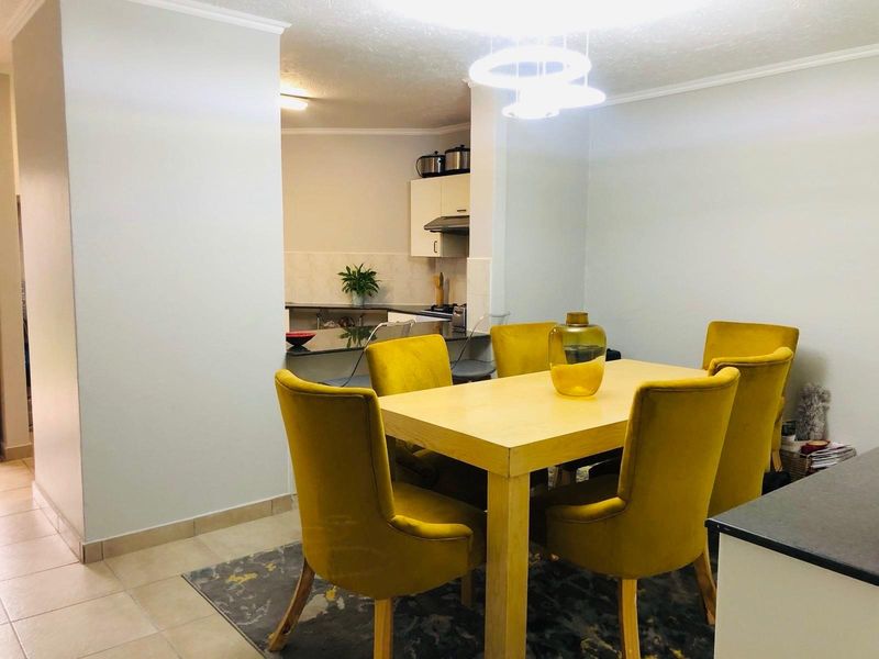 Open plan dining area adjacent to a functional kitchen with built-in cabinetry and tiled flooring.