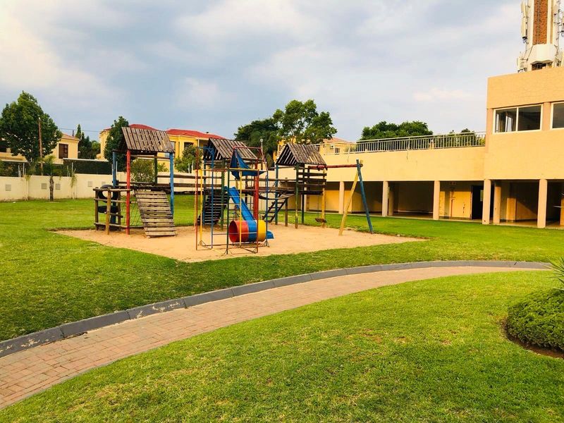 Communal garden area featuring a children's playground, paved walkway, and access to the apartment building's ground floor exterior.