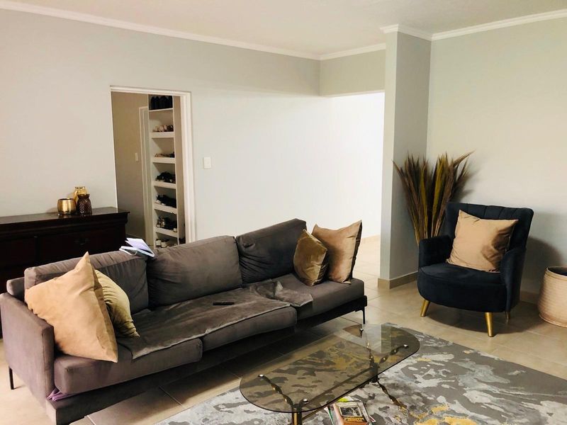 A comfortable living room featuring neutral wall tones, tiled flooring, and a doorway leading to a built-in shelving unit or storage area.