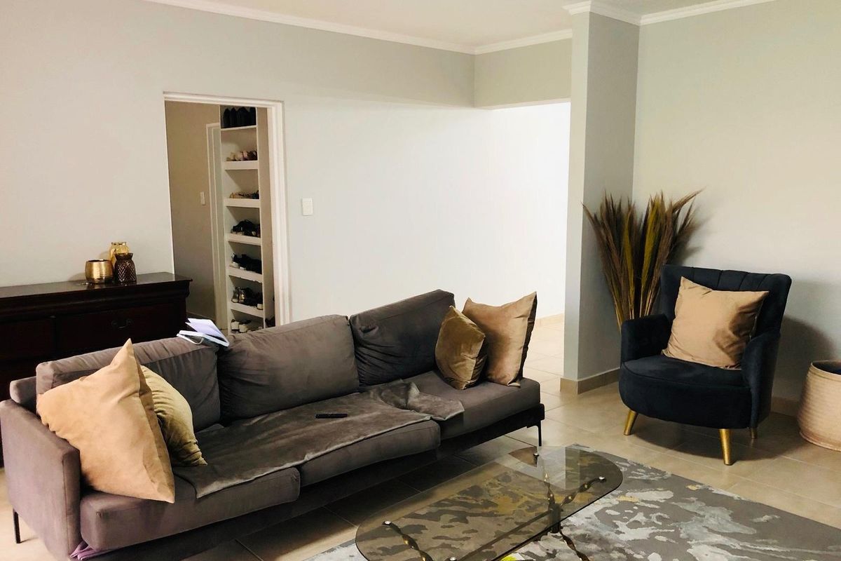 A comfortable living room featuring neutral wall tones, tiled flooring, and a doorway leading to a built-in shelving unit or storage area.