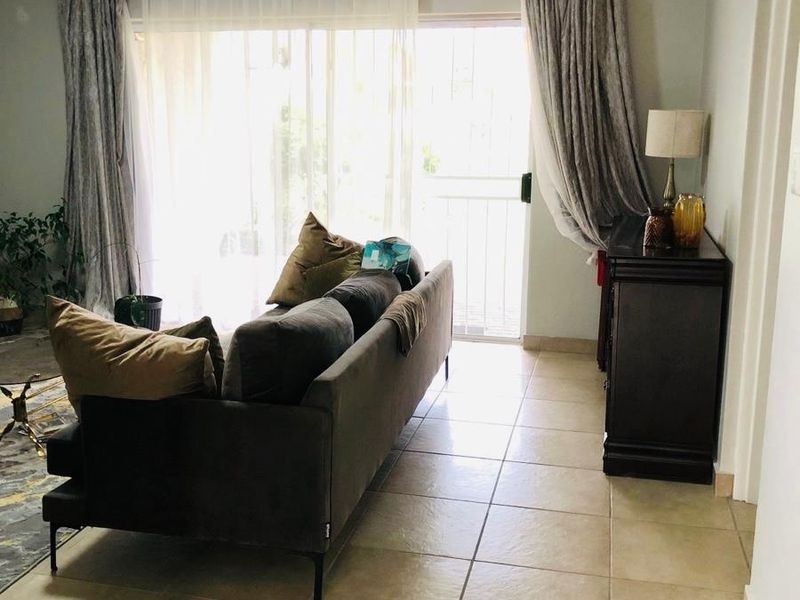A bright living room featuring large sliding glass doors that open onto a balcony, finished with neutral floor tiles.